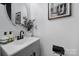 Elegant powder room with a modern oval mirror, sleek black faucet, and a decorative vase at 2656 Grantham Place Dr, Fort Mill, SC 29715