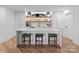 Modern basement bar features sleek white cabinetry, wooden shelves, and three stools at the quartz countertop at 16439 Jetton Rd, Cornelius, NC 28031