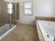 Bright bathroom featuring a glass shower and soaking tub, tiled floors, and a large window at 12326 Cranberry Glades Dr, Cornelius, NC 28031