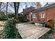 View of a brick home exterior with a wood deck, mature trees, and partial shade in the backyard at 1831 Jameston Dr, Charlotte, NC 28209