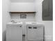Clean laundry room with white front-load washer and dryer, floating wooden shelf, and gray flooring at 360 Patience Dr, Concord, NC 28025