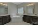 Luxurious bathroom featuring a garden tub, dark wood vanities with granite countertops, and tile flooring at 17809 Pawleys Plantation Ln, Charlotte, NC 28278