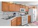 Well-lit kitchen featuring wood cabinets, white appliances, stylish backsplash, and a double sink at 2592 Brackley Nw Pl, Concord, NC 28027