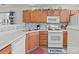 Efficient kitchen featuring wood cabinets, white appliances, mosaic backsplash, and a stainless steel sink at 2592 Brackley Nw Pl, Concord, NC 28027