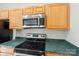 Kitchen featuring stainless steel microwave and black stove top set over green countertop with matching wood cabinets at 3010 Uxbridge Woods Ct, Charlotte, NC 28205