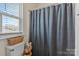 Small bathroom with a toilet, shower with gray shower curtain, blinds on a window and a small storage container at 7200 Irongate Dr, Lancaster, SC 29720