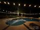 Sparkling in-ground pool at night with string lights overhead and lush landscaping at 17048 Jetton Rd, Cornelius, NC 28031