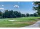 Scenic view of the lush golf course with green fairways, a sand trap, and trees under a blue sky at 19622 River Falls Dr, Davidson, NC 28036