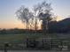 A green field, dark trees, and an orange and yellow sunset beyond a dark metal fence at 485 Harper Miller Dr, Cleveland, NC 27013