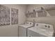 Bright laundry room with white washer and dryer, shelving, and decorative art at 8073 Kennesaw Dr, Gastonia, NC 28056