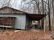 Exterior of metal building with covered area, with stacked wood and overgrown weeds at 2211 Unionville Indian Trl, Indian Trail, NC 28079