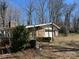 View of the back of the home with a two-car garage, overgrown foliage, and a brick chimney at 2211 Unionville Indian Trl, Indian Trail, NC 28079