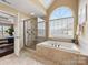 This primary bathroom boasts an enclosed shower, soaking tub, and a large arched window at 5501 Two Iron Dr, Matthews, NC 28104