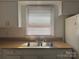 Close-up of kitchen sink with wooden countertop, window, and white cabinetry at 2210 Milton Rd, Charlotte, NC 28215