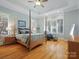 Bright main bedroom featuring a four-poster bed, tray ceiling, plantation shutters, and hardwood floors at 8416 Highgrove St, Charlotte, NC 28277