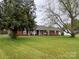 Charming brick home featuring a covered porch and a spacious front yard with mature trees, set against a cloudy sky at 30 Hillsboro Rd, Taylorsville, NC 28681