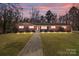 Charming brick ranch-style home with a walkway, illuminated by landscape lighting at dusk, and a well-manicured lawn at 407 Pinecroft Ln, Spencer, NC 28159