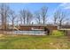 A backyard features a swimming pool, wood deck, black metal fence, and mature trees against a blue sky at 822 Bethlehem Rd, Kings Mountain, NC 28086