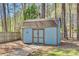 Exterior shot of a small, well-maintained blue storage shed with a shingled roof and wooden double doors at 6688 Pine Forest Dr, York, SC 29745