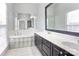 Bathroom featuring a double vanity with dark cabinets, a soaking tub, and a glass block window at 105 Partridge Bluff Ne Dr, Concord, NC 28025