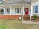 Inviting front porch with a brick base, red front door, and white swing for relaxing and enjoying the outdoors at 2602 Cherokee Ct, Gastonia, NC 28056