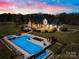 A dusk aerial view of a backyard pool area, including a hot tub, sauna, lounge chairs, and waterfall feature at 12613 Oak Grove Rd, Stanfield, NC 28163