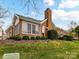 Brick home exterior featuring a chimney, well-manicured landscaping, and a sunroom with large windows at 11406 Olde Turnbury Ct, Charlotte, NC 28277