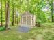 Tan storage shed with double doors and a gravel pathway, nestled among trees in the backyard of the property at 821 Lynnwood Farms Dr, Fort Mill, SC 29715