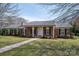 A brick home with a covered front porch, black shutters, and mature trees and landscaping at 104 N Hawthorne St, Mount Holly, NC 28120