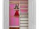 Close-up of closet with custom organizers, gold bars, pink-striped wallpaper, and hanging dresses at 1347 Eisenhower Nw Pl, Concord, NC 28027