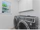 Laundry room with modern washer and dryer, storage cabinets, and bright window at 1347 Eisenhower Nw Pl, Concord, NC 28027