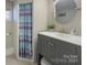 Updated bathroom showcasing a gray vanity, round mirror, and a shower with a striped curtain at 7611 Buckland Rd, Charlotte, NC 28278