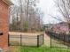 Fenced backyard featuring an iron gate, green grass, and mature trees beyond the property line at 3516 Araglin Dr, Gastonia, NC 28056