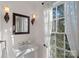 Powder room features a pedestal sink with bronze fixtures, decorative sconces, mirror, and window with decorative curtains at 1624 Chadmore Nw Ln, Concord, NC 28027