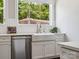 Close-up of a farmhouse sink with white cabinets, stainless steel dishwasher, and natural light from a window above at 317 Old Town Village Rd, Waxhaw, NC 28173
