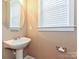 Powder room featuring a pedestal sink, round mirror, and modern fixtures; a clean and bright space at 10133 Caldwell Forest Rd, Charlotte, NC 28213