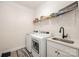 Functional laundry room featuring modern washer and dryer, sink with matte black faucet, and wire shelving at 7056 Cornwallis Ct, Iron Station, NC 28080