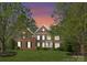 Beautiful brick home featuring mature trees, a manicured lawn, and a stunning sunset sky at 1119 Lytton Ln, Matthews, NC 28104