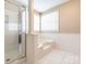 Bright bathroom featuring a tub, a glass-enclosed shower, white tile floor, and wainscoting details at 3274 Roberta Farms Sw Ct, Concord, NC 28027