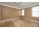 A vacant bedroom with a ceiling fan, two windows, and worn carpeting reveals signs of deferred maintenance and repair at 82 Paddington Sw Dr, Concord, NC 28025