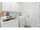 Well-lit laundry room featuring modern white appliances, overhead cabinets, and convenient door at 111 Harris Farm Rd, Mooresville, NC 28115