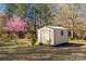 Tan storage shed with metal roof is surrounded by trees and a flowering tree in the yard at 1139 Suttle Rd, Lancaster, SC 29720