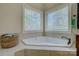 Corner bathtub with tile surround, basket of towels, and bright window with blind coverings for privacy at 17733 Colleton River Ln, Charlotte, NC 28278