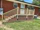 Brick home backyard featuring wooden stairs and railings, lush green grass, and mature foliage at 213 Crowell Ave, Albemarle, NC 28001