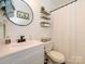 Well-lit bathroom with a white vanity, modern fixtures, toilet, and shower with storage shelves at 2518 Eargle Rd, Charlotte, NC 28269