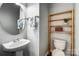 Well-lit half bathroom featuring a pedestal sink, modern fixtures, and wooden shelves for storage at 5807 Mctaggart Ln, Charlotte, NC 28269