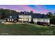 A stunning exterior shot of a large home with a manicured lawn, brick accents, and many windows glowing in the evening light at 447 Willow Pond Ln, Hiddenite, NC 28636