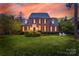 Stately brick home with manicured lawn and two chairs on the front lawn at sunset at 7700 Red Oak Ln, Charlotte, NC 28226