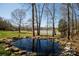 Landscaped pond with stone edging, mature trees, and nearby outbuildings at 4229 Motocross Trl, Edgemoor, SC 29712
