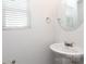 Modern powder room with white pedestal sink, round mirror, and window with blinds, creating a clean and bright space at 8232 Waxhaw Hwy, Waxhaw, NC 29173